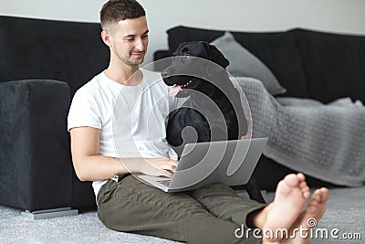 Freelancer guy with laptop and dog is working at home in quarantine to coronavirus infection Stock Photo