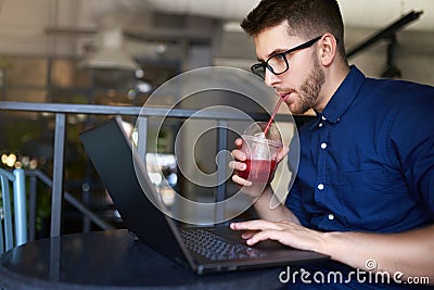 Freelancer man with plastic cup of fresh beverage in hand works with laptop. Businessman in glasses drinks juice for Stock Photo
