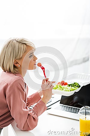 Freelancer sitting near laptop and eating cherry tomato Stock Photo