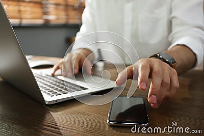 Freelancer taking smartphone while working on laptop at table indoors, closeup Stock Photo