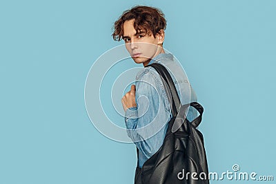 Freestyle. Man in denim shirt with backpack standing isolated on gray looking back close-up Stock Photo