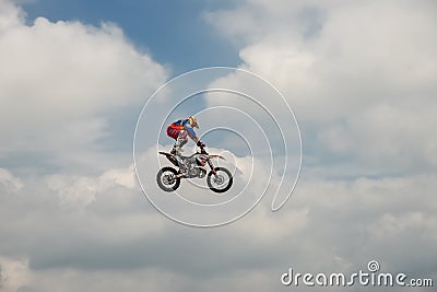 Freestyle Motocross rider carries out a trick with the motorcycle on background of the blue cloud sky. Extreme sport. German-Stunt Editorial Stock Photo