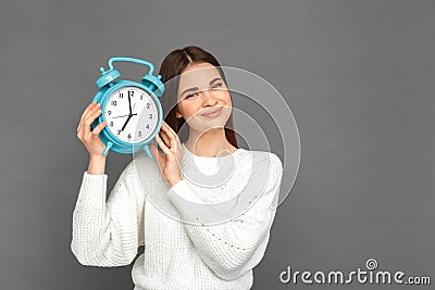 Freestyle. Young girl standing on grey with clock listening to ticking smiling cheerful Stock Photo