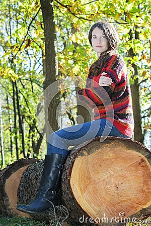 Freezing woman sitting on sawn tree trunk and hugging herself Stock Photo