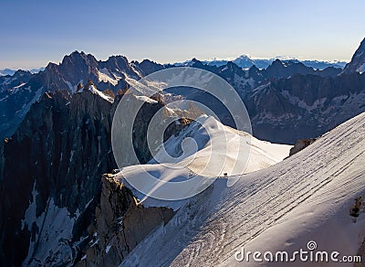 French Alps mountains peaks panorama view with silhouettes of climbers as roping team descending on the snowy slope under Aiguille Stock Photo