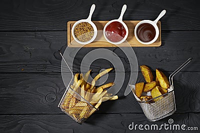 French fries and country potatoes in a basket and three different sauces: Ketchup, Mustard and Barbecue on dark background, top Stock Photo