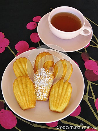 French madeleines and tea in pink vintage dishware on black and magenta cherry-pattern tablecloth Stock Photo