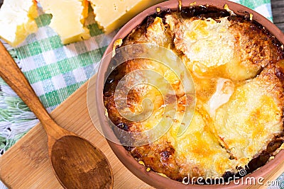 French onion gratin soup in a clay pot, authentic recipe, wooden spoon on a cutting board on an old rustic table, close-up Stock Photo