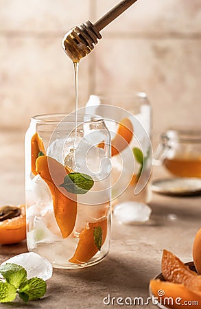 Fresh apricot cocktail, fizz or ice tea with mint and garnish, process of adding honey. Pink beige tile background Stock Photo