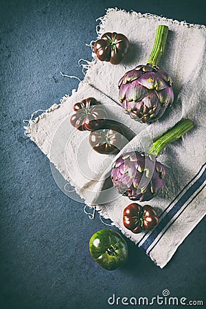 Fresh artichokes, green and black tomatoes on linen textile. Flat lay Stock Photo