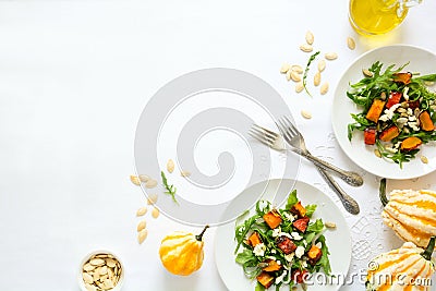 Fresh autumn salad with baked pumpkin, arugula, cheese and seeds on white table cloth Stock Photo