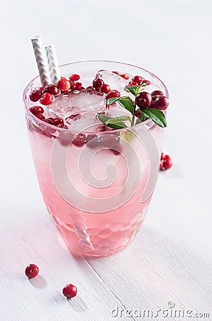 Fresh beverage berry drink with red lingonberry and green leaves in sunbeam on white wooden board, vertical, closeup. Stock Photo