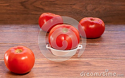Fresh big red tomato on a white ceramic plate and more tomatoes in background Stock Photo