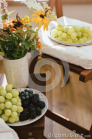 Fresh blueberries, blackberries and grapes in sunlight and wildflowers bouquet in rustic room. Summer berries in light, healthy Stock Photo