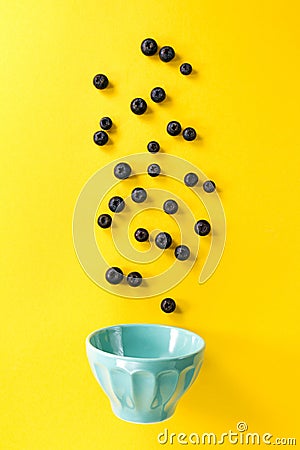 Fresh blueberries flying to blue bowl on yellow background. Food Stock Photo