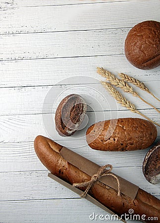 Fresh bread - buns, baguette and ears of wheat on wooden background flat lay. Vertival image Stock Photo