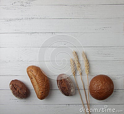 Fresh bread - buns, baguette and ears of wheat on wooden background flat lay. Vertival image Stock Photo