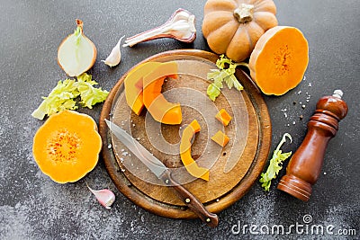 Fresh bright cutted pumpkin on a wooden chopping board with knife. Celery and garlic, onions and scattered peppercorns and salt Stock Photo