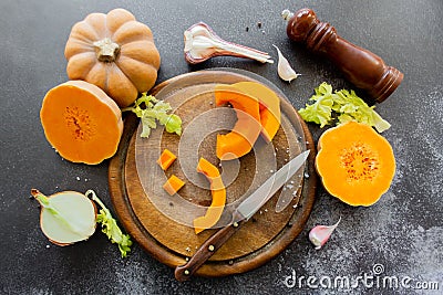 Fresh bright cutted pumpkin on a wooden chopping board with a knife. Celery and garlic, onions and scattered peppercorns and salt Stock Photo
