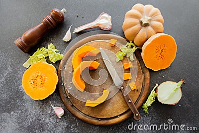 Fresh bright cutted pumpkin on a wooden chopping board with a knife. Celery and garlic, onions and scattered peppercorns and salt Stock Photo