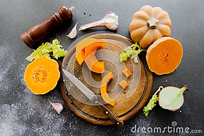 Fresh bright cutted pumpkin on a wooden chopping board with knife. Celery and garlic, onions and scattered peppercorns and salt Stock Photo