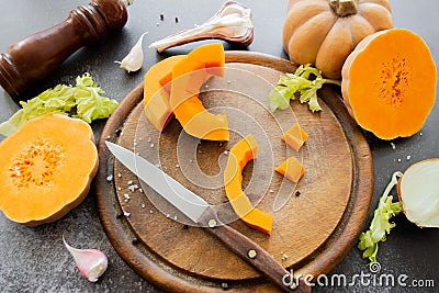 Fresh bright cutted pumpkin on a wooden chopping board with knife. Celery and garlic, onions and scattered peppercorns and salt Stock Photo