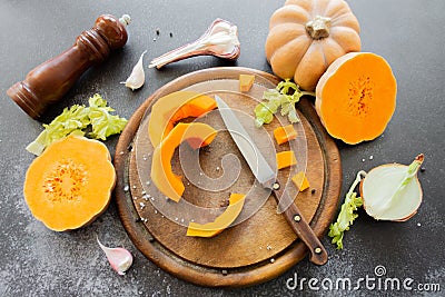 Fresh bright cutted pumpkin on a wooden chopping board with knife. Celery and garlic, onions and scattered peppercorns and salt Stock Photo