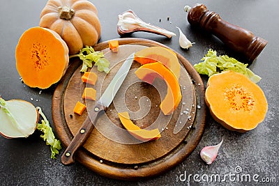 Fresh bright cutted pumpkin on a wooden chopping board with knife. Celery and garlic, onions and scattered peppercorns and salt Stock Photo