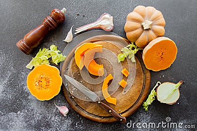 Fresh bright cutted pumpkin on a wooden chopping board with a knife. Celery and garlic, onions and scattered peppercorns and salt Stock Photo