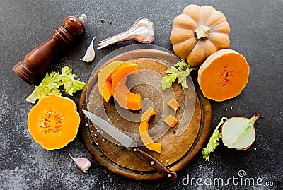 Fresh bright cutted pumpkin on a wooden chopping board with a knife. Celery and garlic, onions and scattered peppercorns and salt Stock Photo