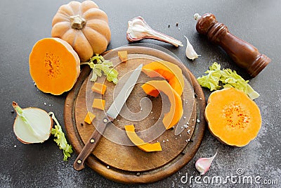 Fresh bright cutted pumpkin on a wooden chopping board with a knife. Celery and garlic, onions and scattered peppercorns and salt Stock Photo