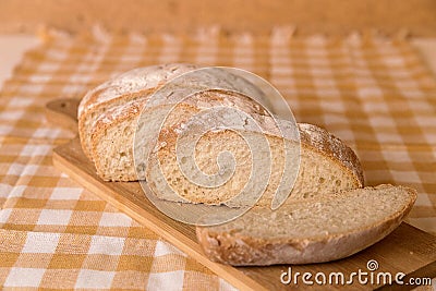 Fresh chabata bread cut into pieces on a wooden board, yellow towel Stock Photo