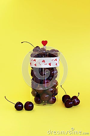 Fresh cherry berries in a glass jug isolated on a yellow background Stock Photo