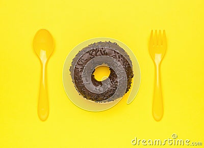 Fresh chocolate donut, yellow spoon and fork on a yellow background. The minimal concept of popular baking Stock Photo