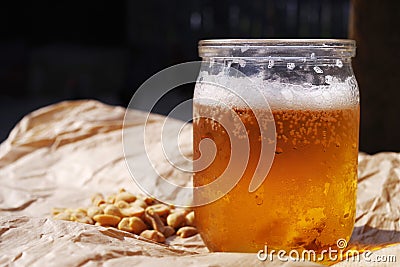 Fresh cold beer in a half liter glass jar and nuts on crumpled paper. Stock Photo