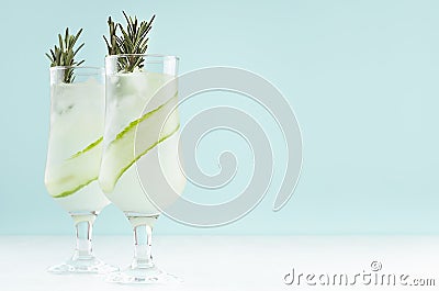 Fresh cool lemonade of cucumber with ice cubes, rosemary, lime in two wineglasses on white and pastel green background, copy space Stock Photo