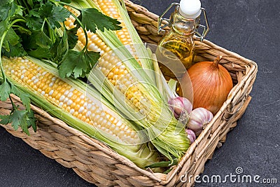 Fresh corn cobs, green parsley, oil in bottle, and garlic in wicker basket Stock Photo