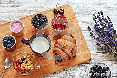 Fresh croissant, berries, yogurt, cornflakes and cup of milk on a wooden table. Stock Photo