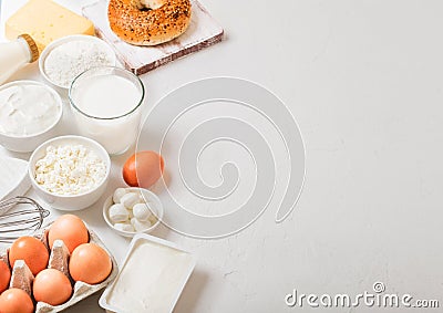 Fresh dairy products on white table background. Glass of milk, bowl of sour cream and cottage cheese and eggs. Fresh baked bagel. Stock Photo
