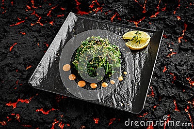 Fresh delicious Chukka seaweed Wakame salad ina black plate on a black stone background with limon and sauce Stock Photo