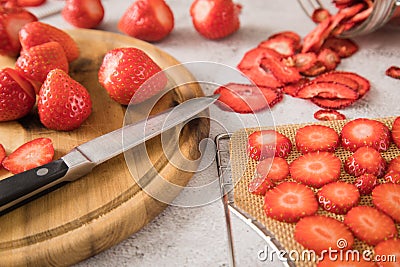 Fresh and dried strawberries from dehydrator for long term prepper pantry with knife, wooden cutting board and glass jar on light Stock Photo