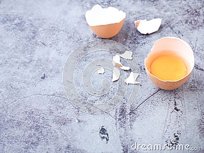 Fresh egg half-cracked with yolk on grey background. High protein and Vitamin foods. Stock Photo