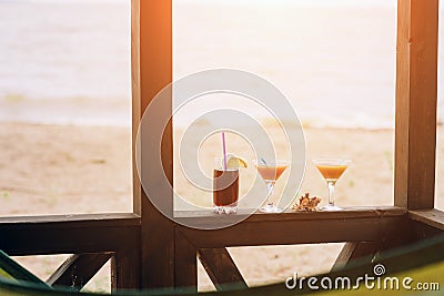 Fresh exotic cocktails on wooden edge. Shell lying between glasses. Cola with straw and lemon. Edge of house. View at Stock Photo