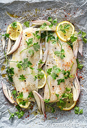 Fresh fish, cod fillets with parsley, lemon slices, onion and spices prepared for baking on parchment paper Stock Photo