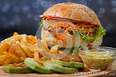Fresh fishburger sandwich, fried potatoes, zucchini, served on wooden plate Stock Photo