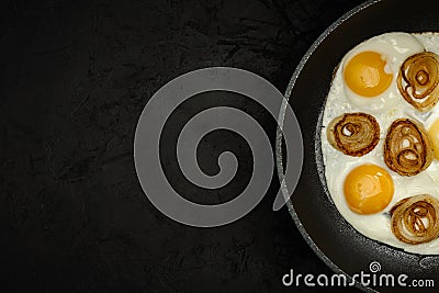 fresh fried eggs with onion rings in a frying pan on a black textured plaster background. top view. artistic dark moody photo with Stock Photo