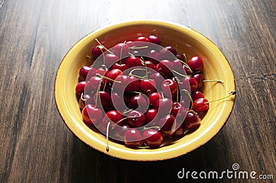 Fresh garden cherries in yellow ceramic bowl on wooden table. Summer harvest. Delicious red berries. Stock Photo