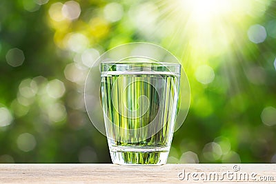 Fresh glass of drinking water on wooden tabletop on blurred green nature bokeh background Stock Photo