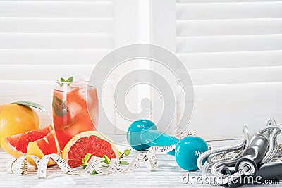 Fresh grapefruits, dumbbell, rope and measuring tape, on rustic white wooden table opposite the blinds, fitne Stock Photo