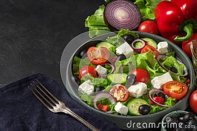 Fresh greek salad with olives, feta cheese, tomato, cucumber, onion with fork on towel on black background Stock Photo
